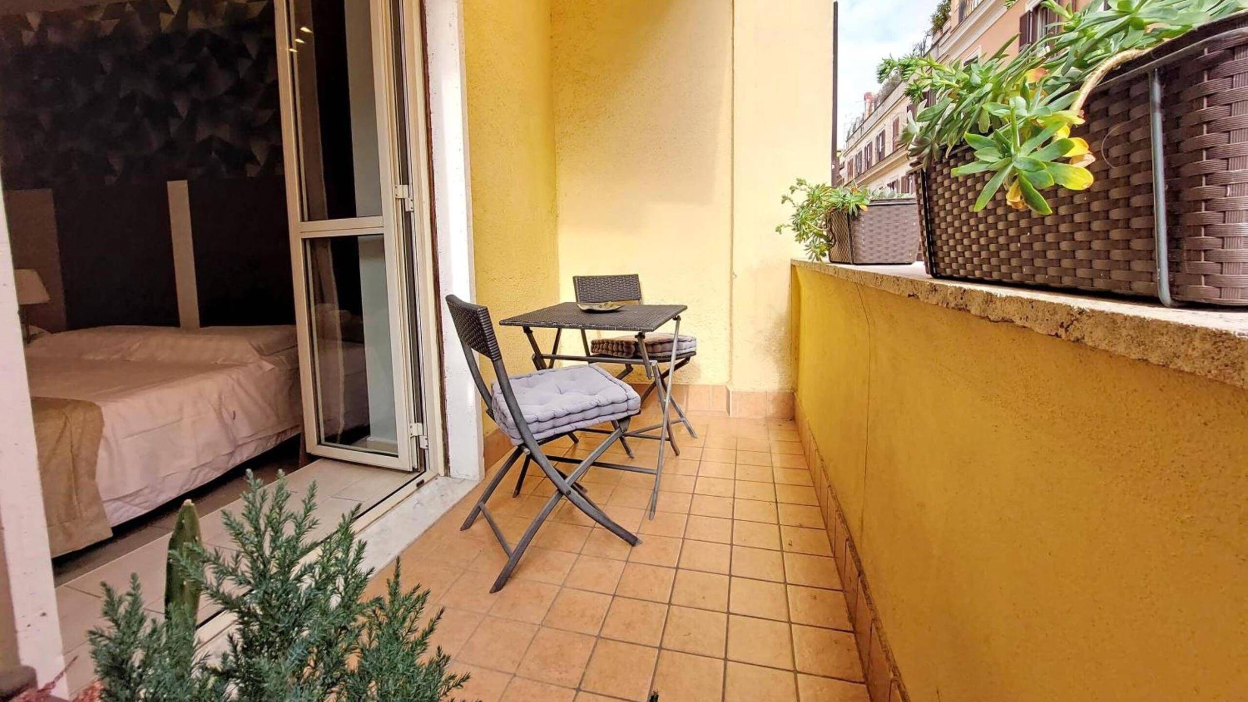 En lille balkon med et bord og stole, en skydedør i glas og en gul væg.