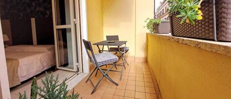 En lille balkon med et bord og stole, en skydedør i glas og en gul væg.
