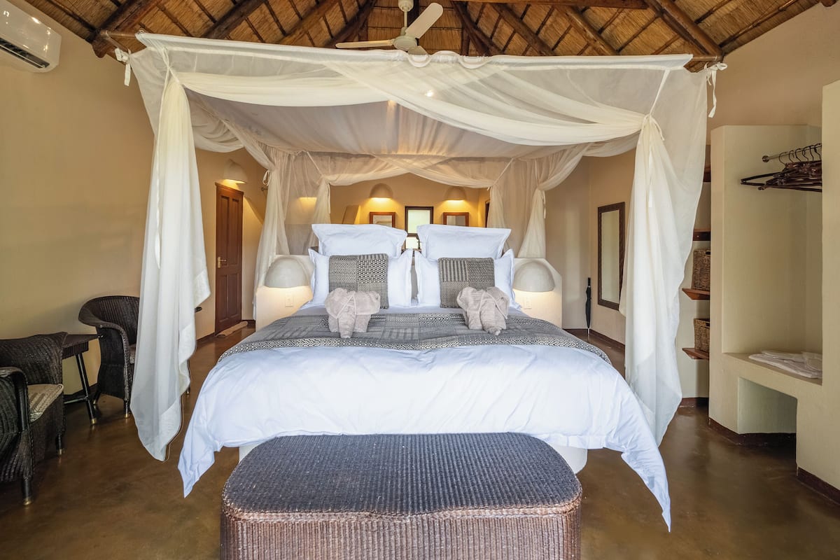 A spacious bedroom with a canopy bed, bedside lamps, wicker furniture, and a ceiling fan.