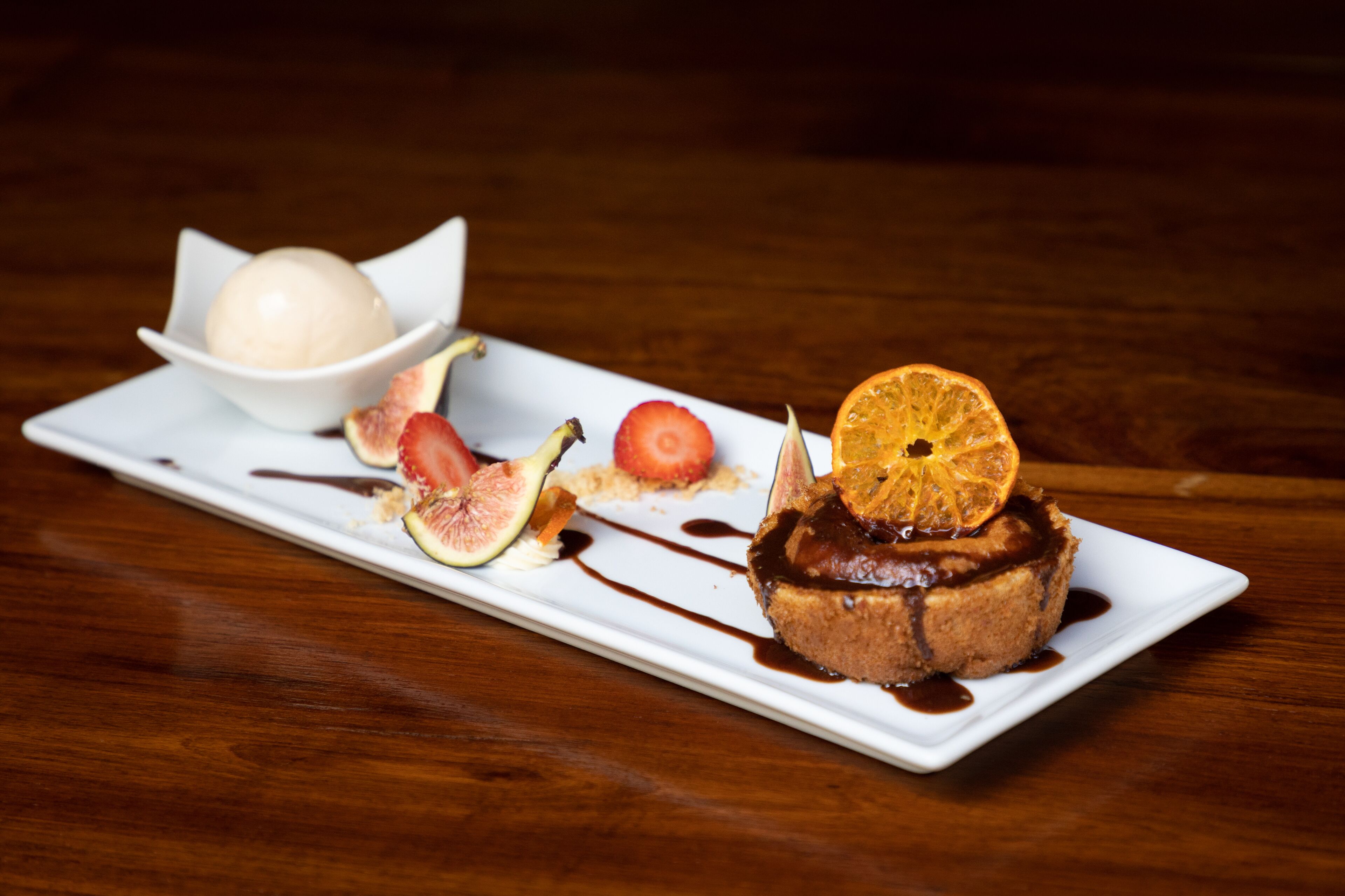 A dessert plate with a chocolate cake topped with an orange slice, figs, and a scoop of ice cream.
