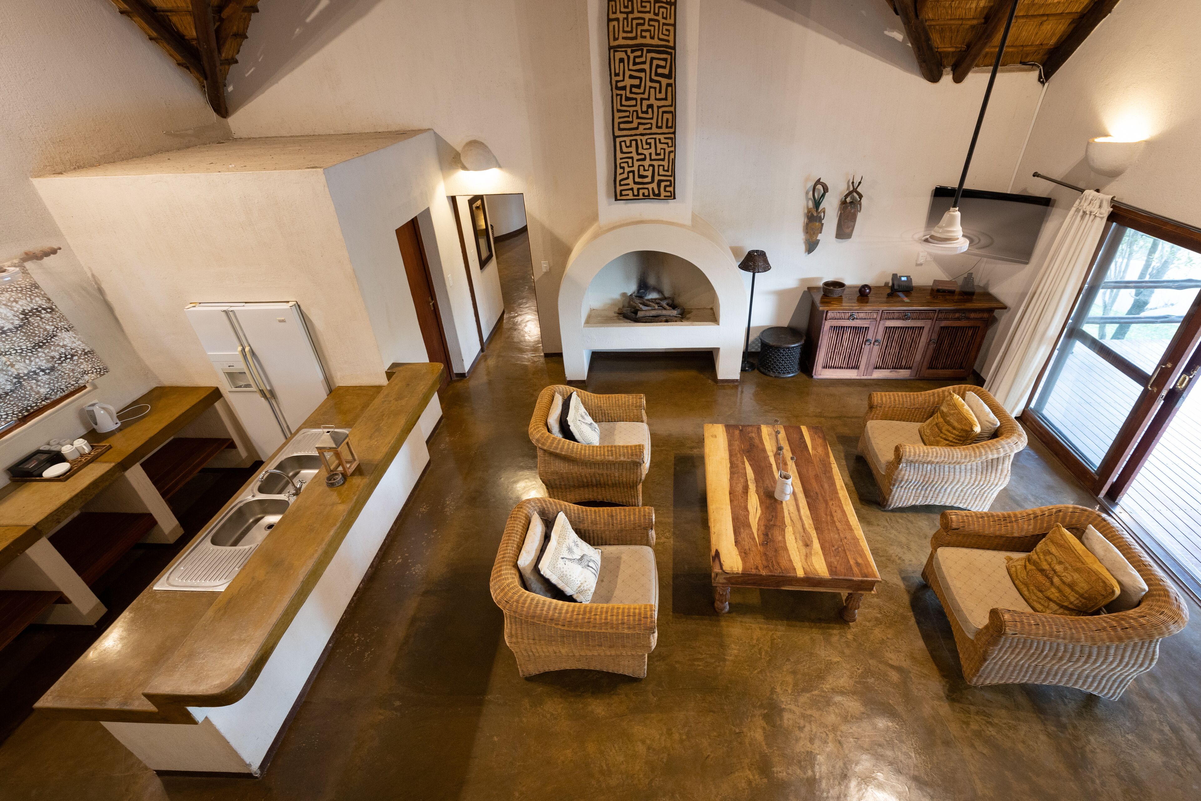 A spacious living area with wicker furniture, a fireplace, and a kitchen with a built-in refrigerator.