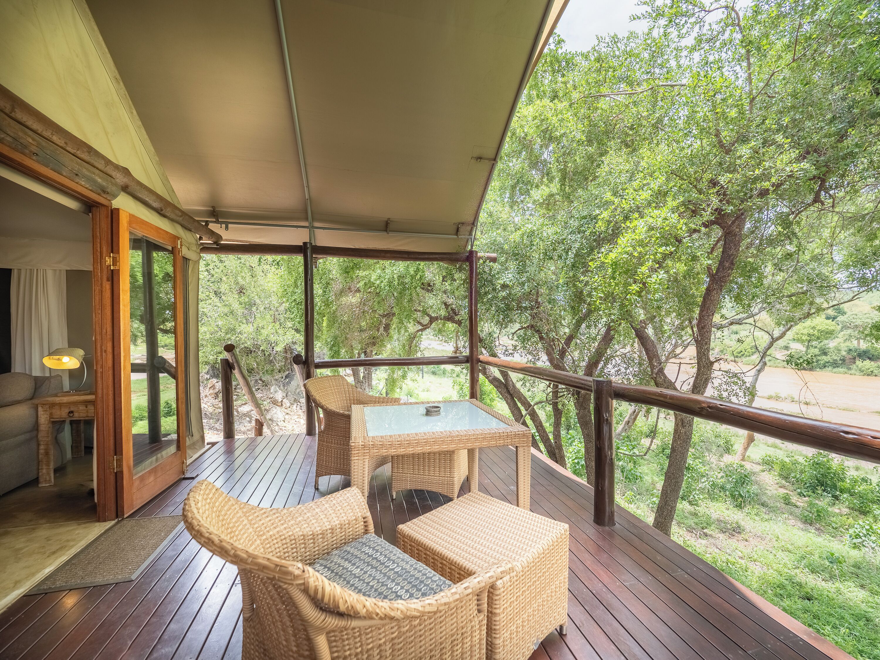 A wooden deck with wicker furniture, a glass door leading outside, and a view of greenery.