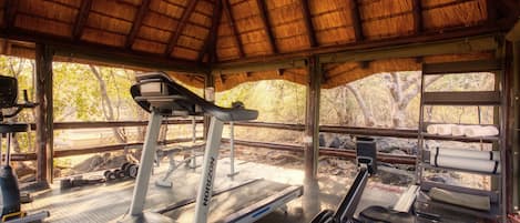 A gym with treadmills and exercise bikes, a thatched roof, and a view of trees.