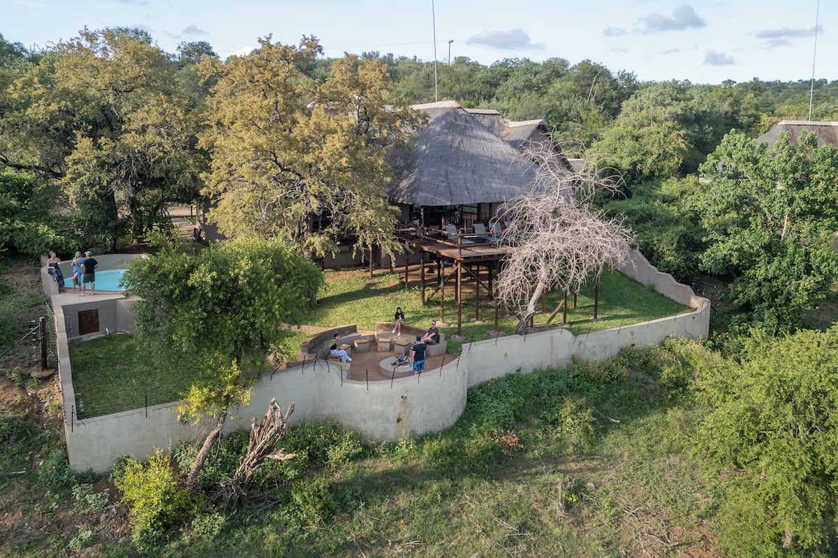 A thatched-roof structure surrounded by lush greenery, with a swimming pool and outdoor seating area.