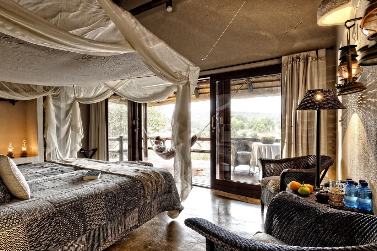Ein Schlafzimmer mit Bett, Stuhl, Tisch und Blick ins Freie.