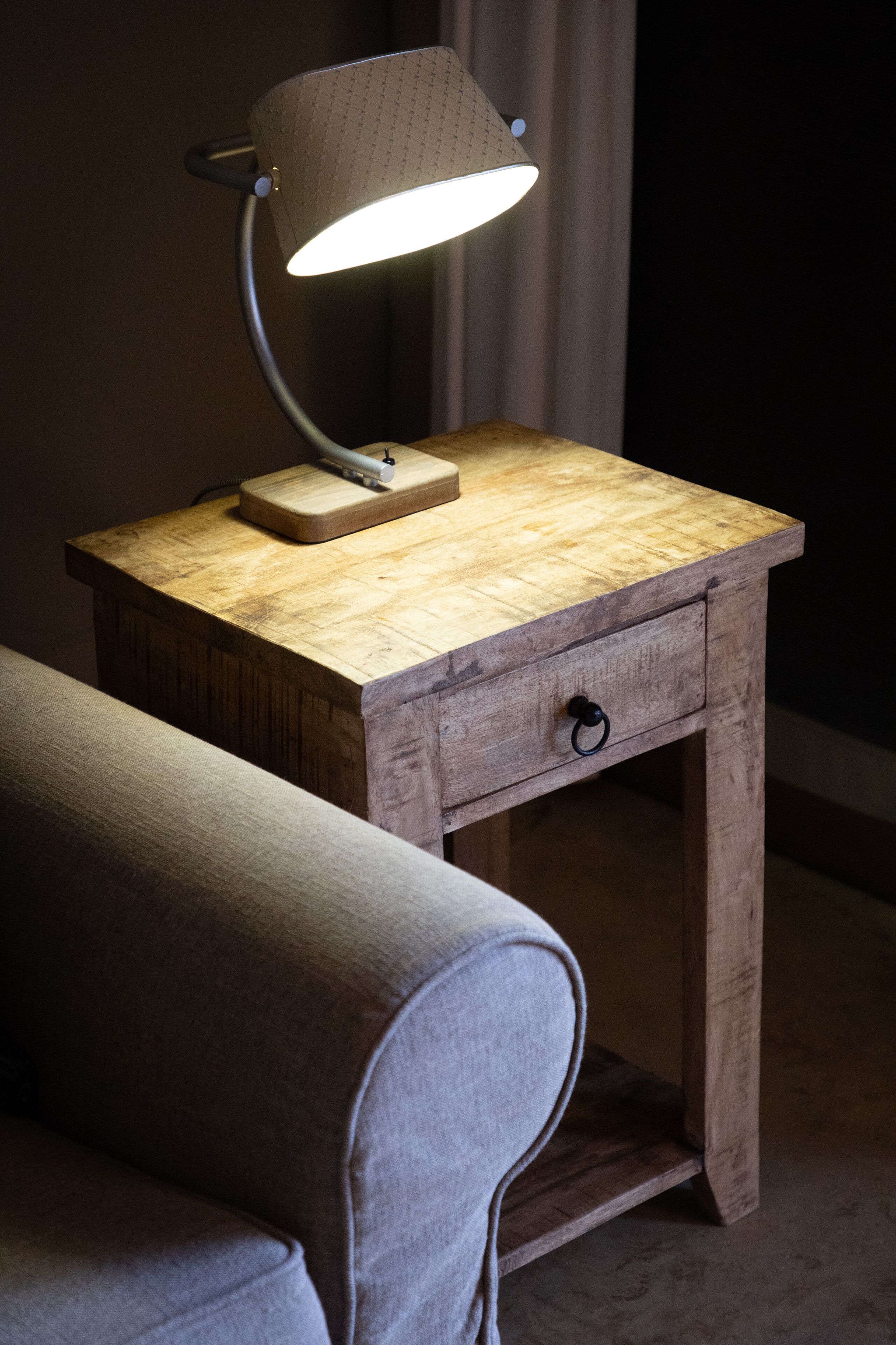 A wooden nightstand with a lamp, a drawer, and a small table.