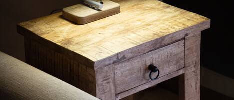 A wooden nightstand with a lamp, a drawer, and a small table.