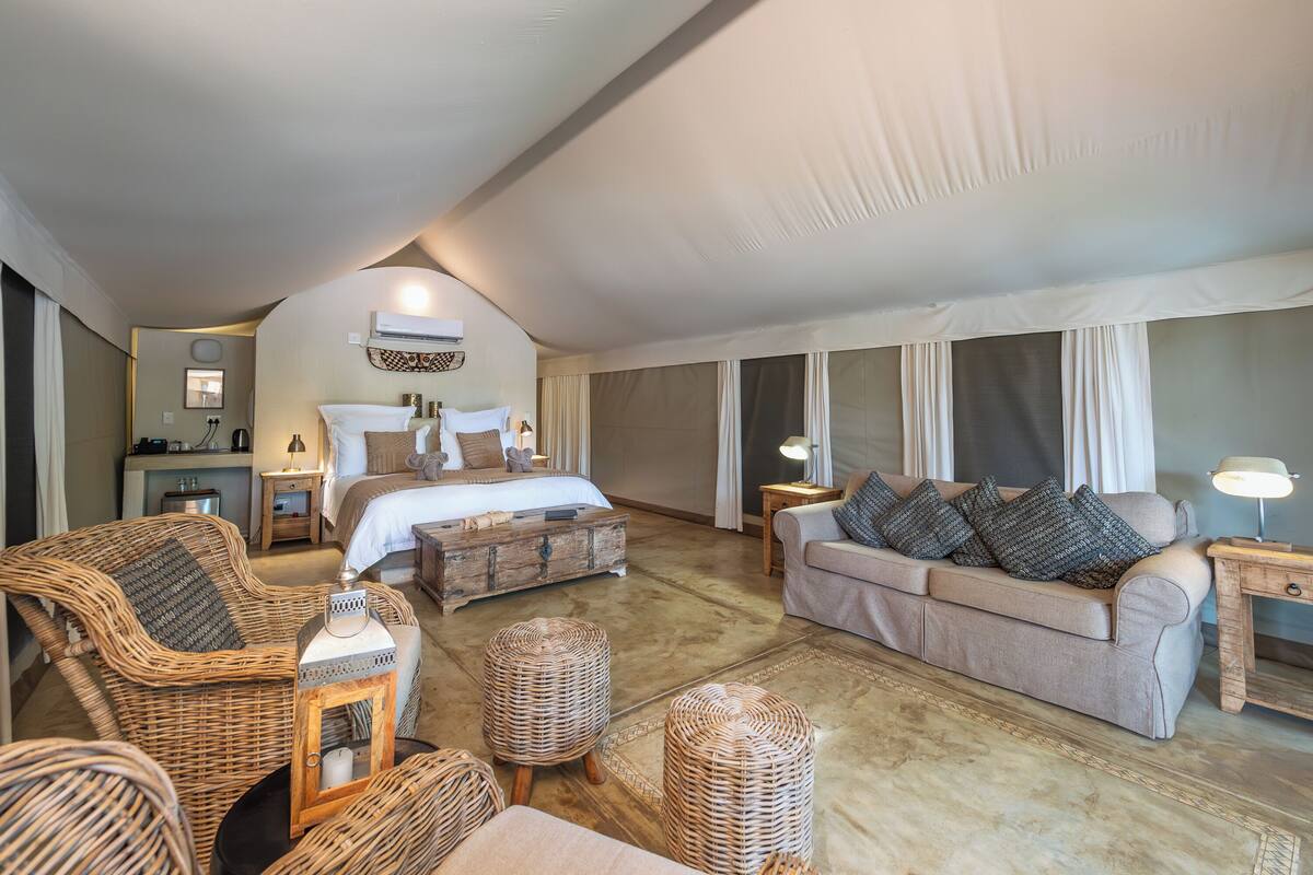 A spacious room with a large bed, a sofa, and a dining table.
