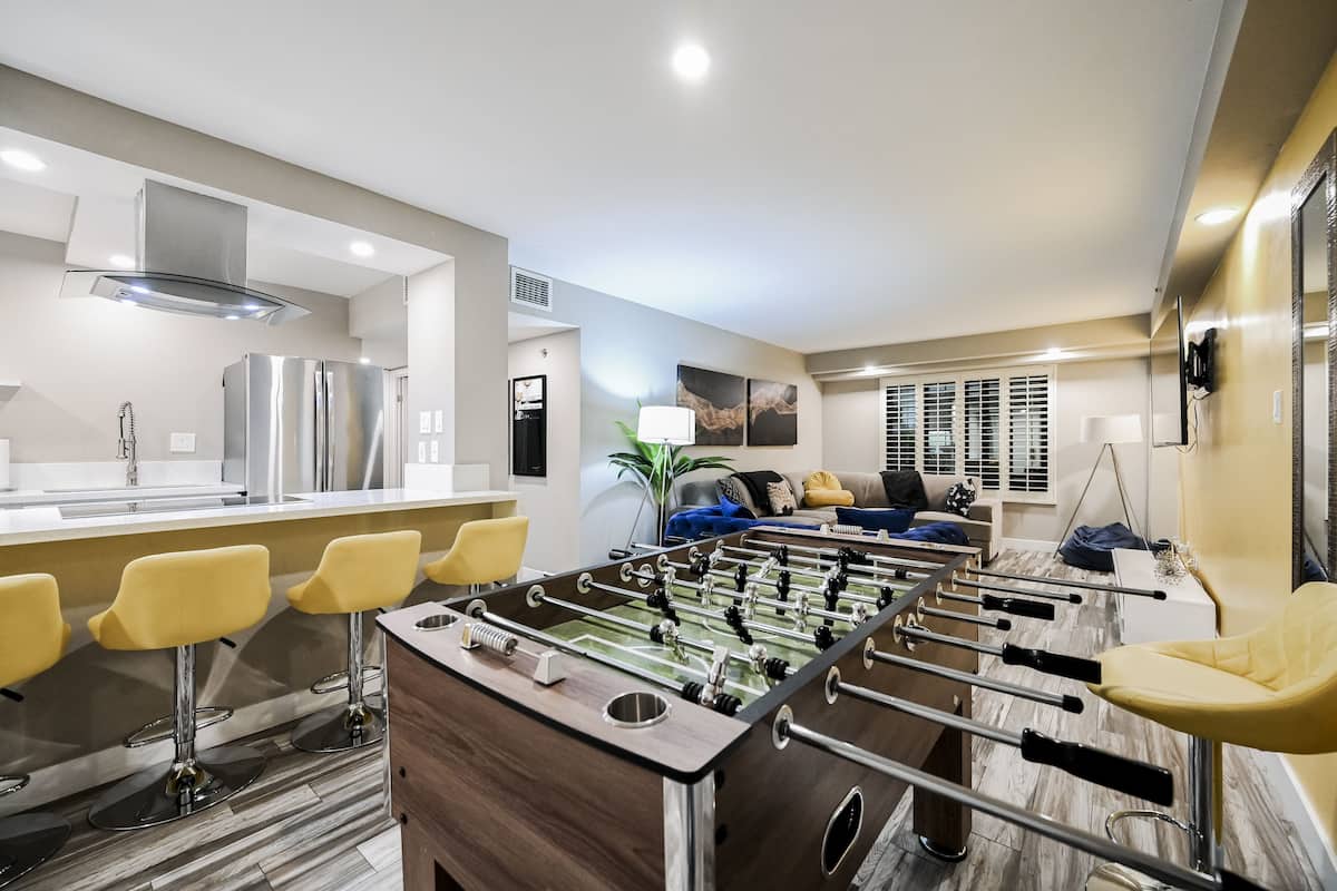 A modern kitchen with a foosball table, bar seating, and a living area with a sofa and decorative items.