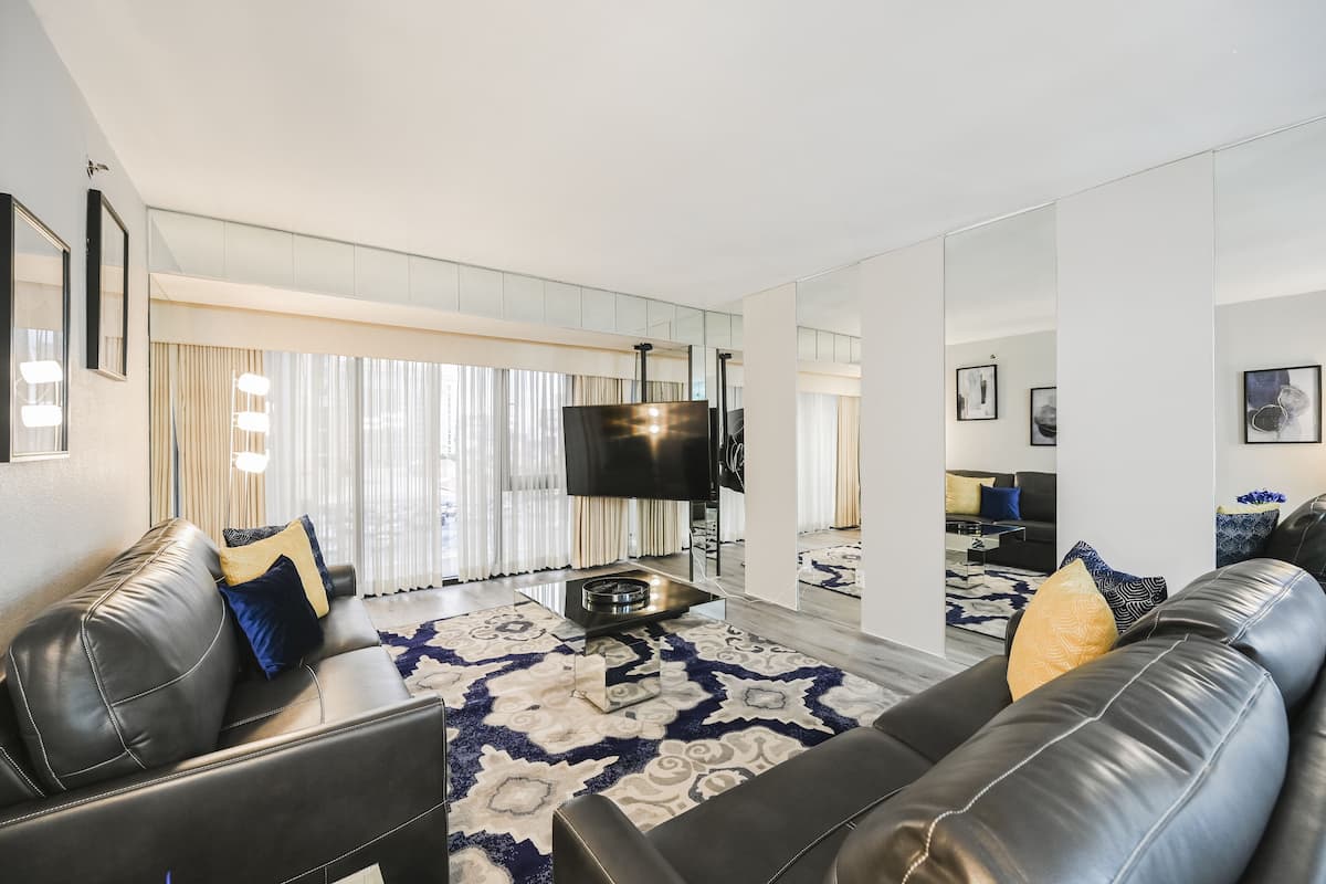 A modern living room with a black leather sofa, a patterned rug, and a flat-screen TV.