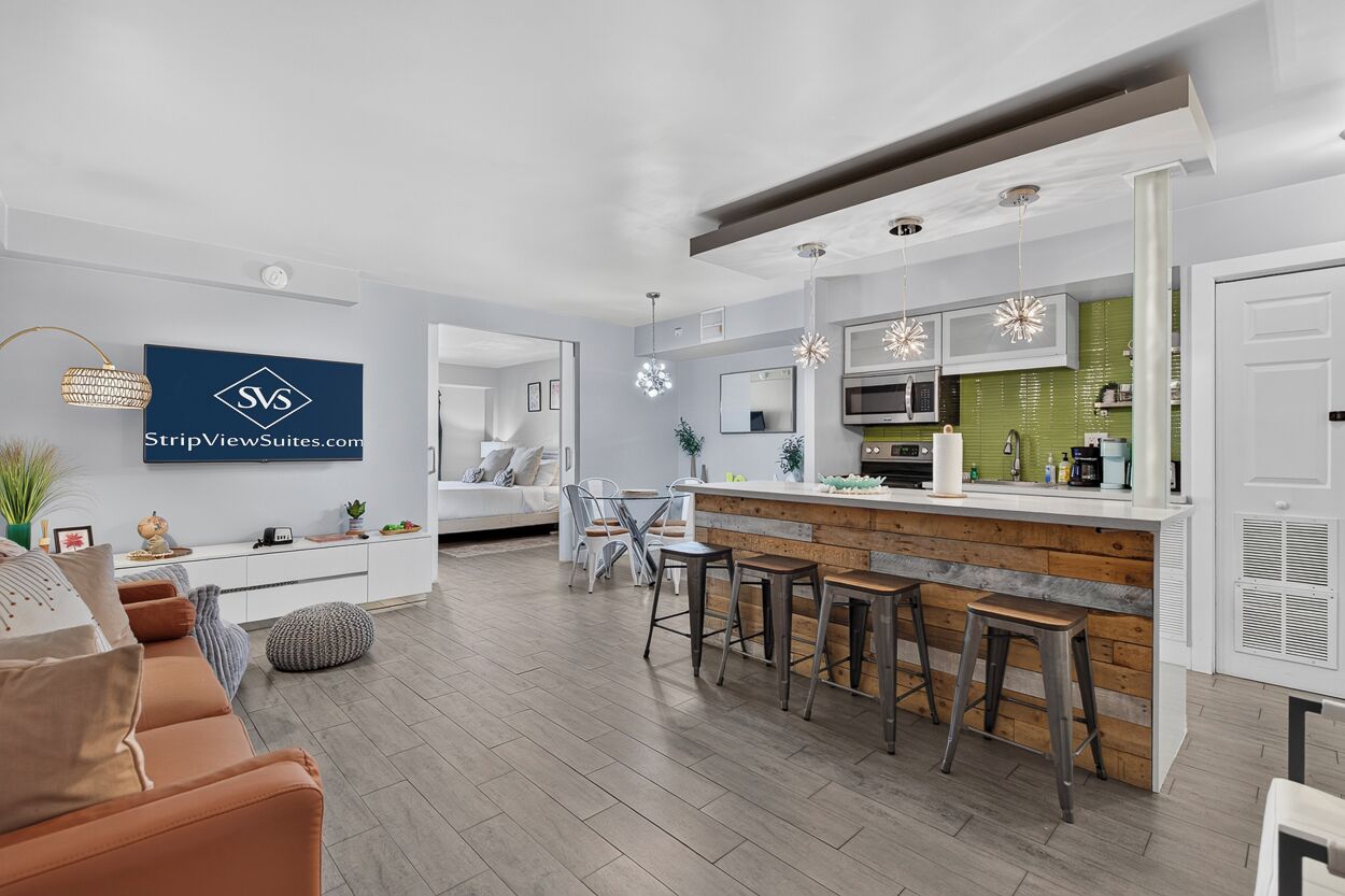A modern kitchen with a bar area, a dining space, and a living area with a sofa and a TV.