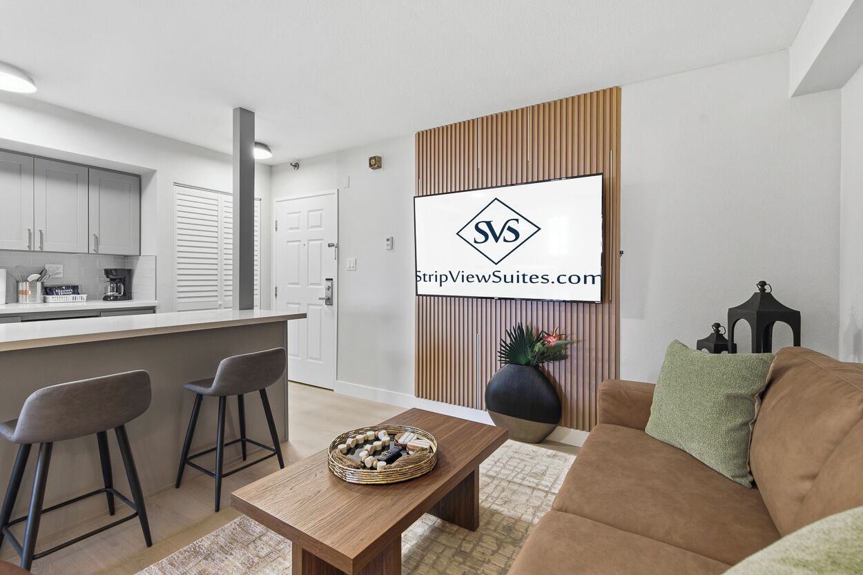 A modern kitchen with white cabinets, a wooden countertop, and a dining area with a table and two bar stools.