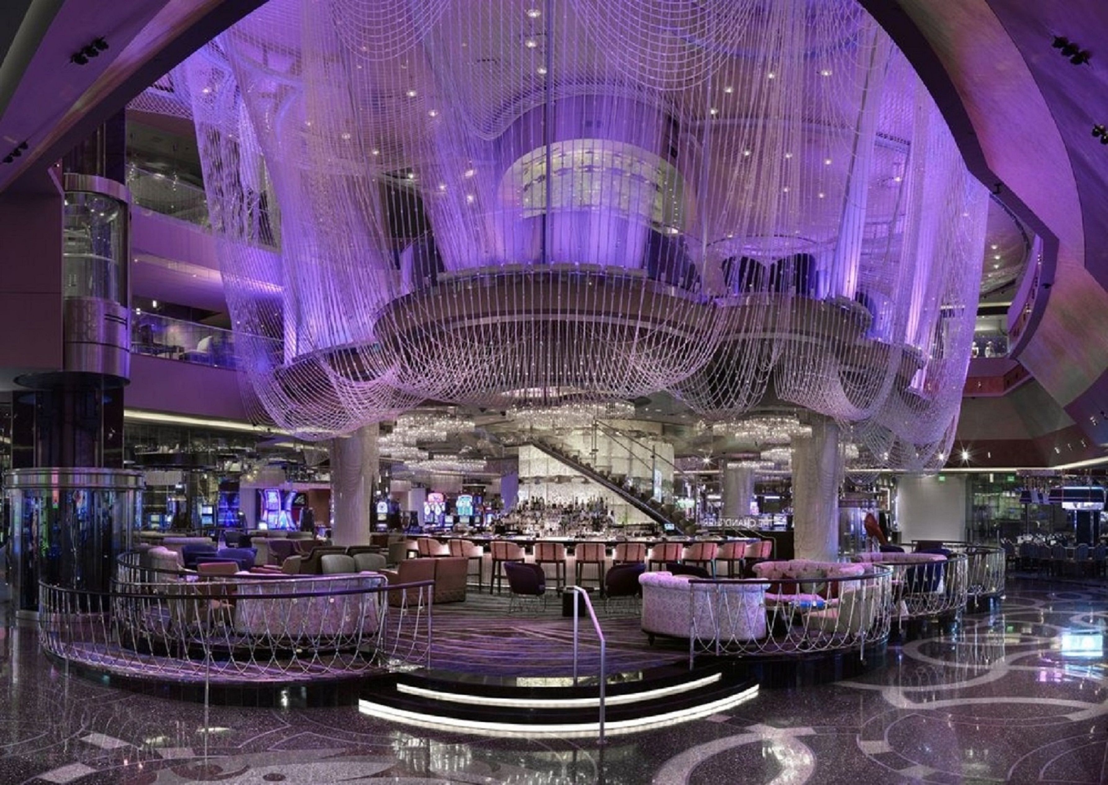 A spacious lobby with a central stage, multiple seating areas, and a modern chandelier.