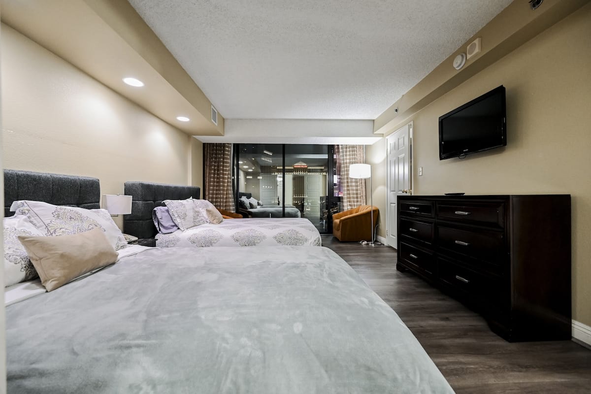 A modern hotel room with a large bed, a television, a dresser, and a seating area with a chair and a table.