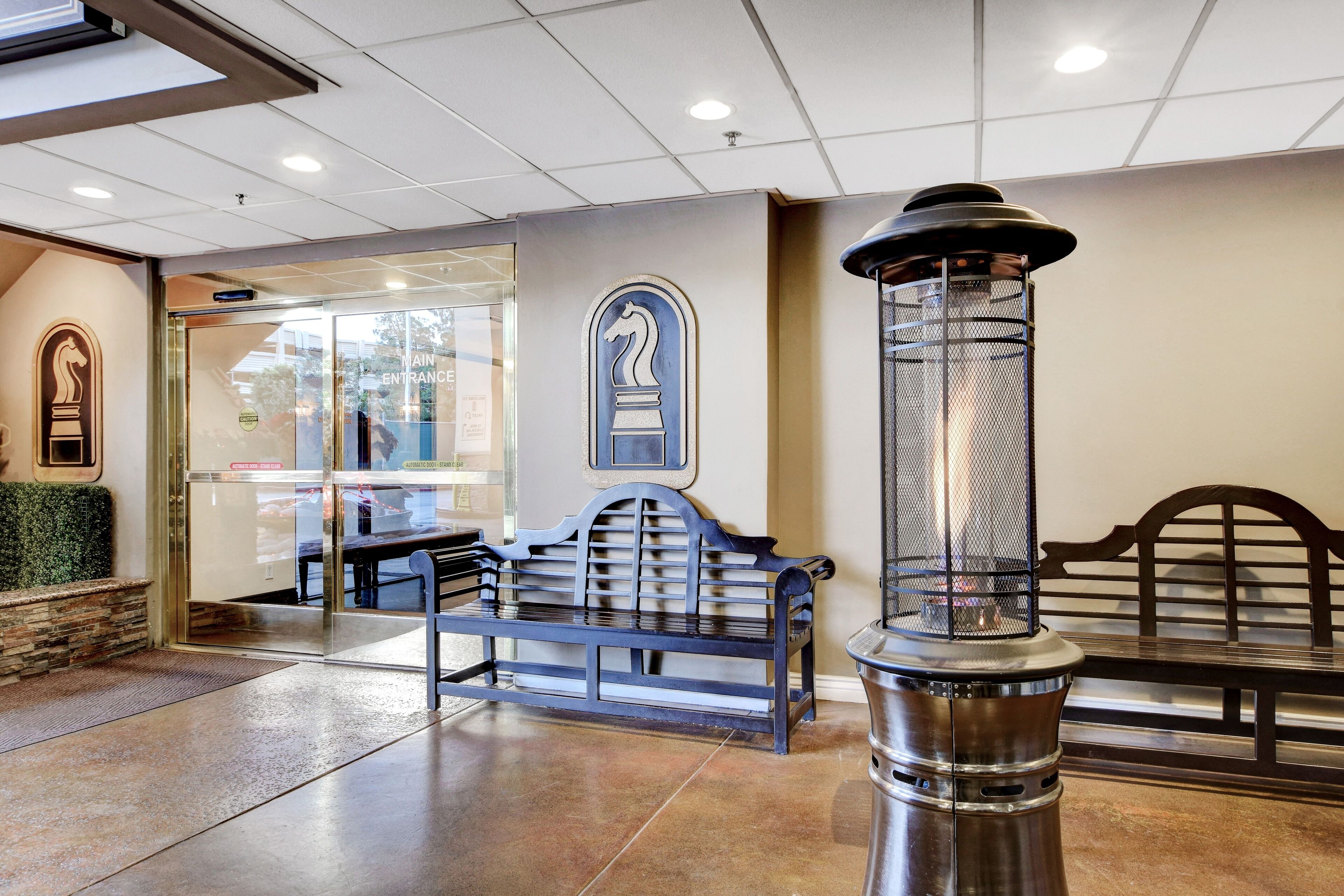 Un vestíbulo con un banco, una columna metálica decorativa y una puerta de vidrio que da a la entrada principal.