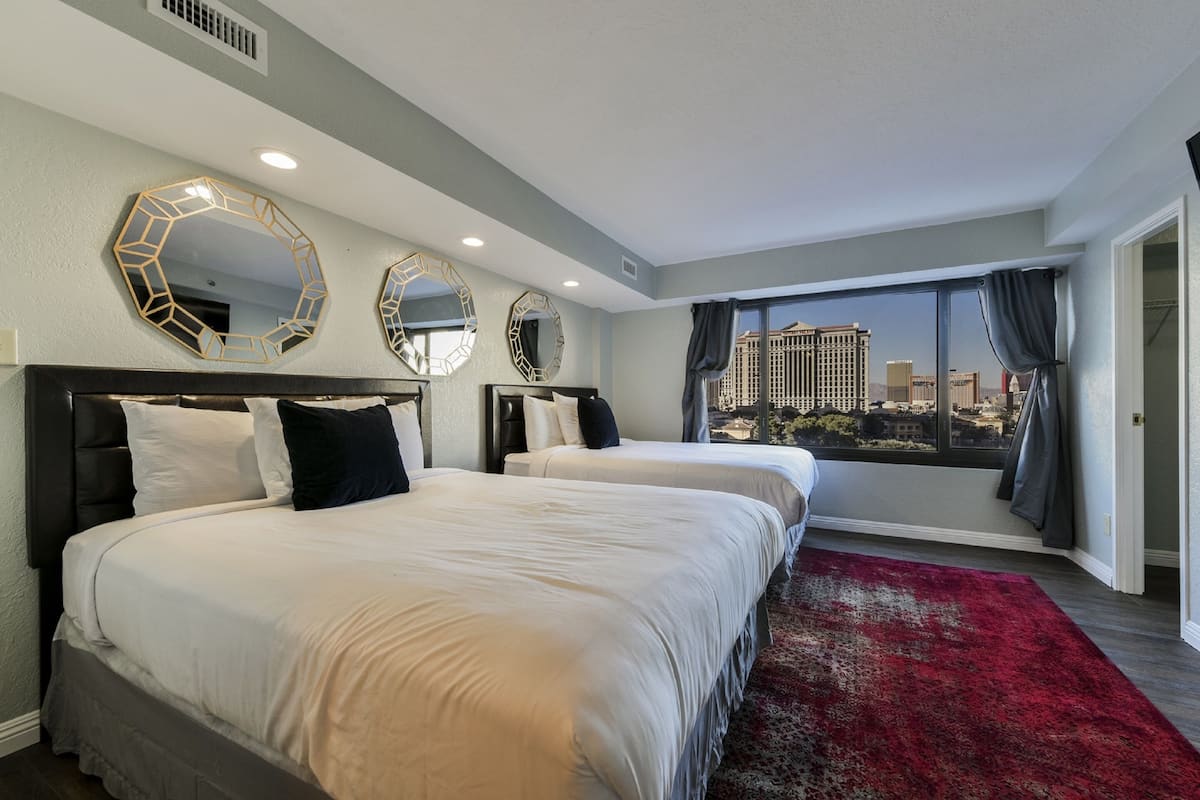 A hotel room with two beds, a red carpet, and large windows with a city view.