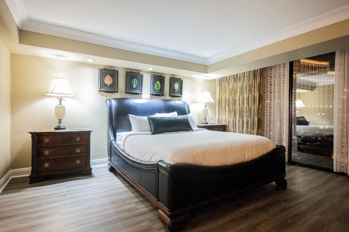 A hotel room with a large bed, wooden nightstands, and a view through a glass door.