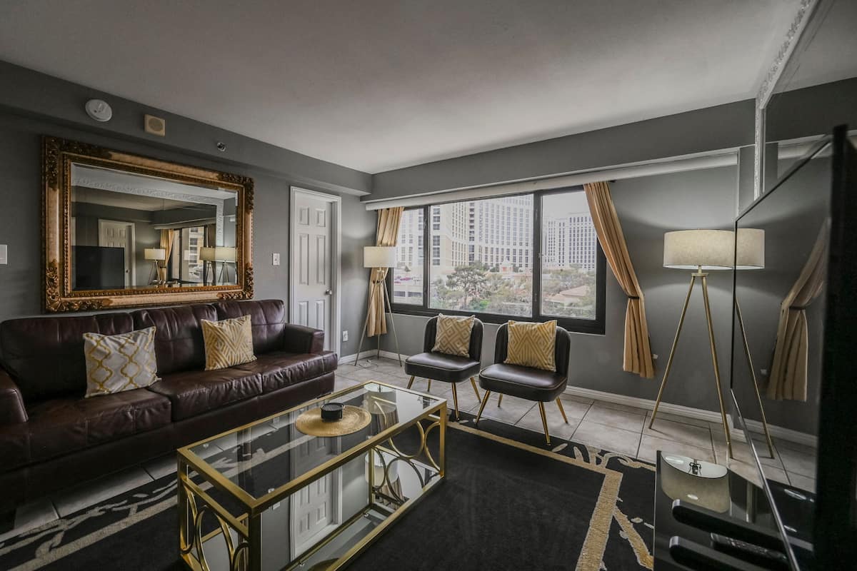 A modern living room with a dark brown leather sofa, two black armchairs, a glass coffee table, and a large mirror.