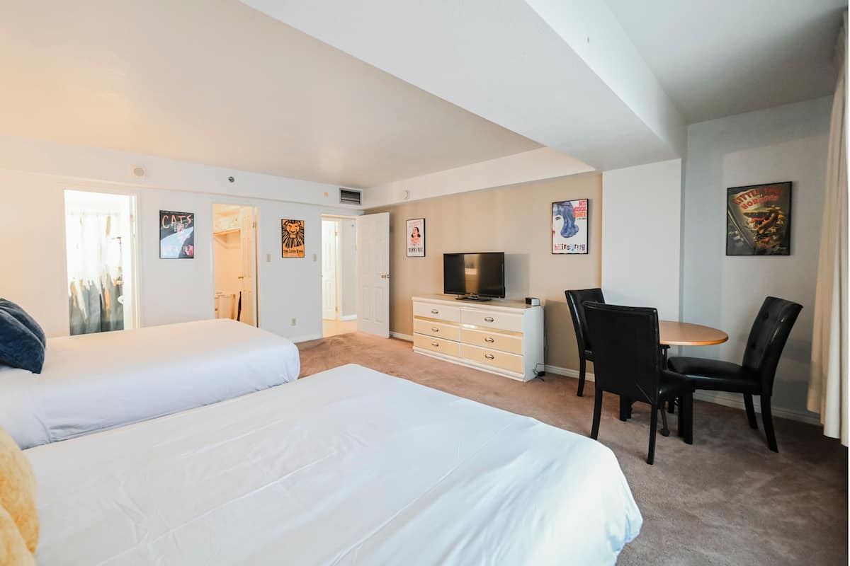A hotel room with two beds, a TV, a desk with a chair, and artwork on the walls.
