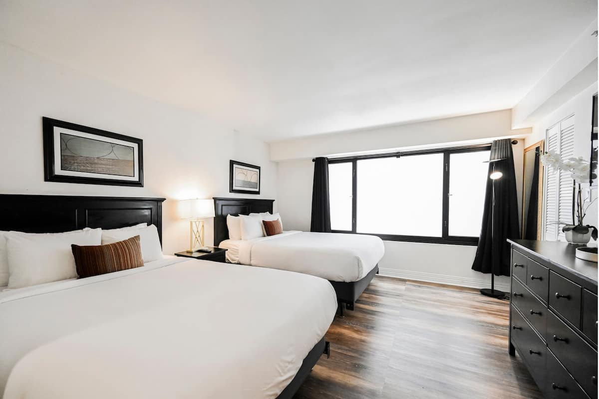 A hotel room with two beds, a large window, a black dresser, and a framed picture on the wall.