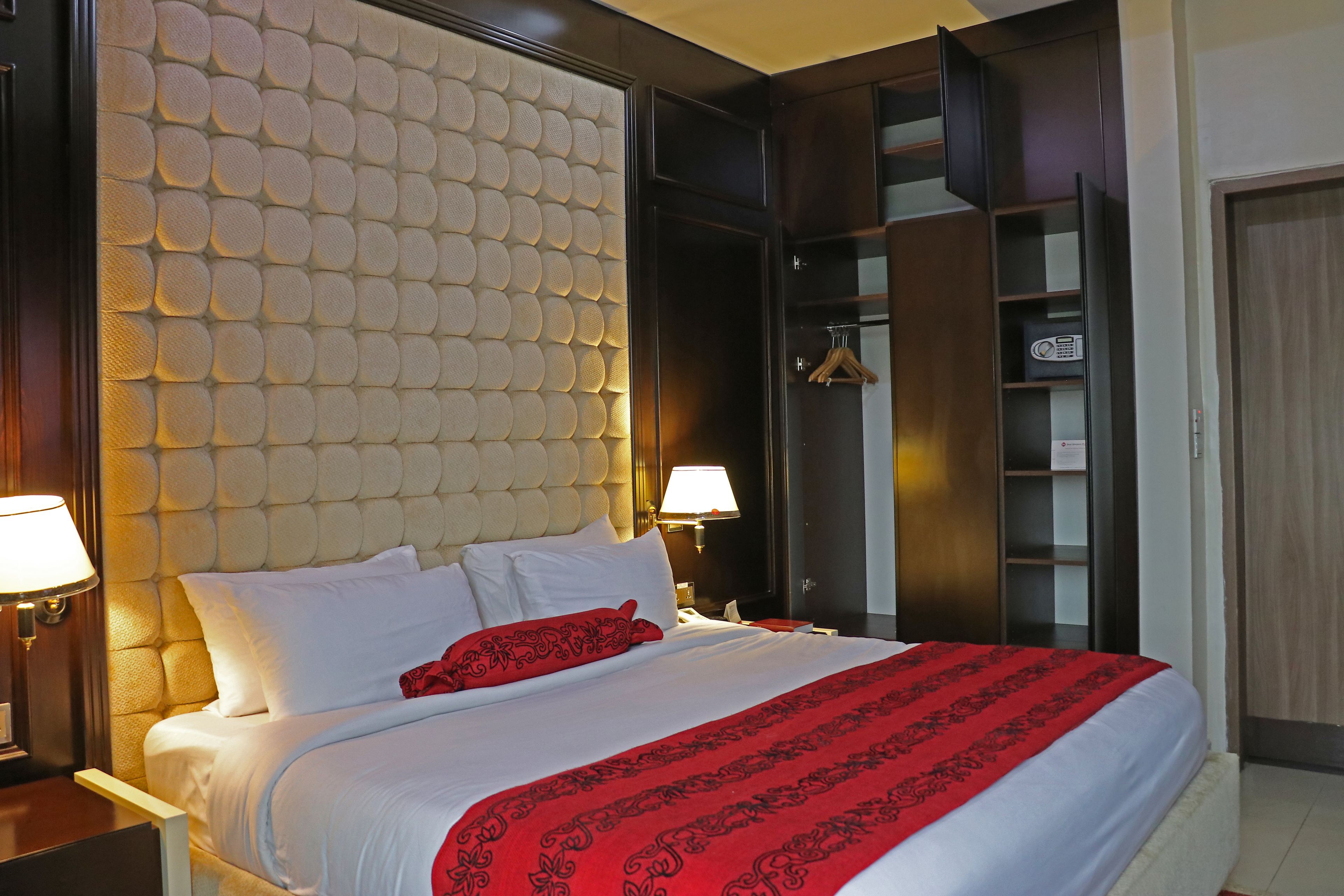 Habitación de hotel con una cama grande, cabecera con diseño texturizado, armario y mesita de noche con lámpara.