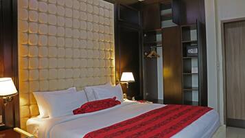 Habitación de hotel con una cama grande, cabecera con diseño texturizado, armario y mesita de noche con lámpara.