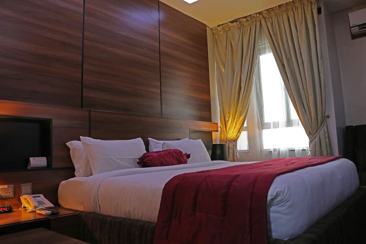 A hotel room with a large bed, a bedside telephone, and a window with curtains.