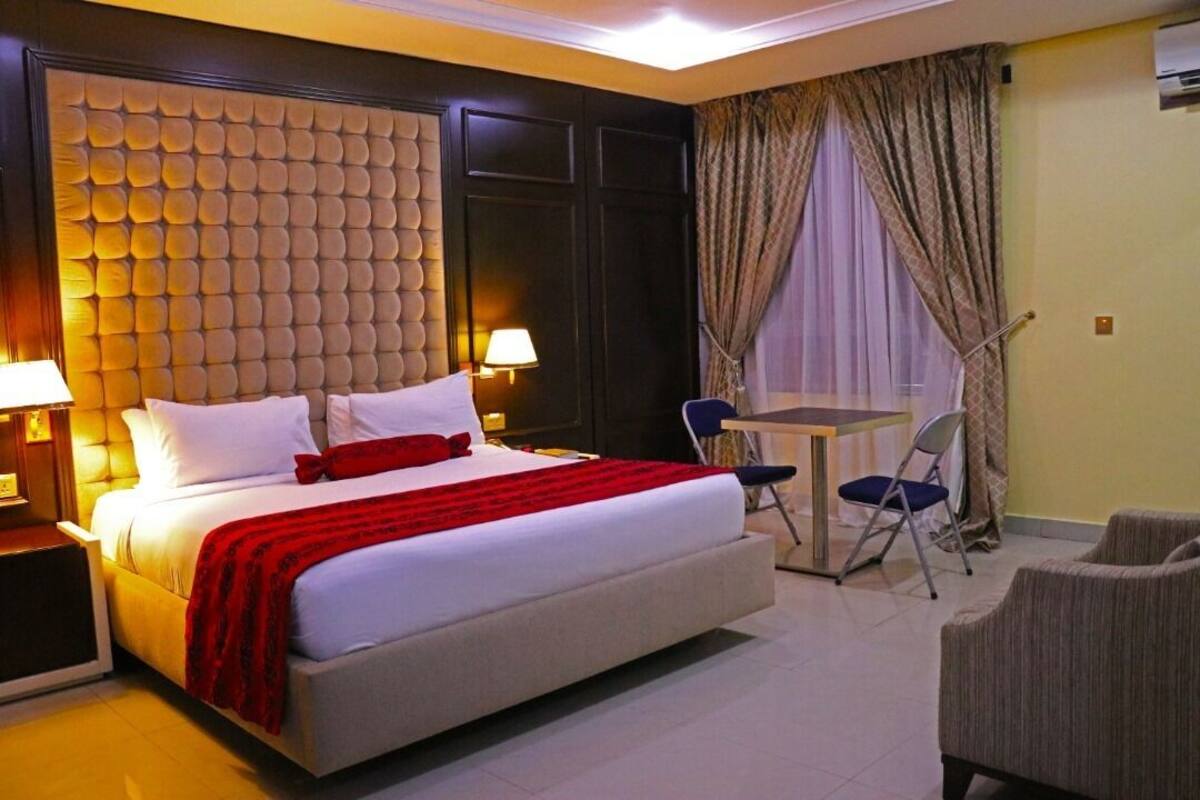 A hotel room with a large bed, a small table with chairs, and a view of the outdoors through curtains.