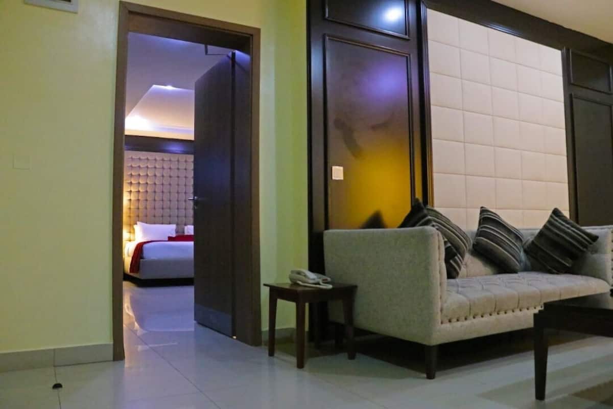 A hotel room with a sofa, a small table, and a bed with a white headboard.