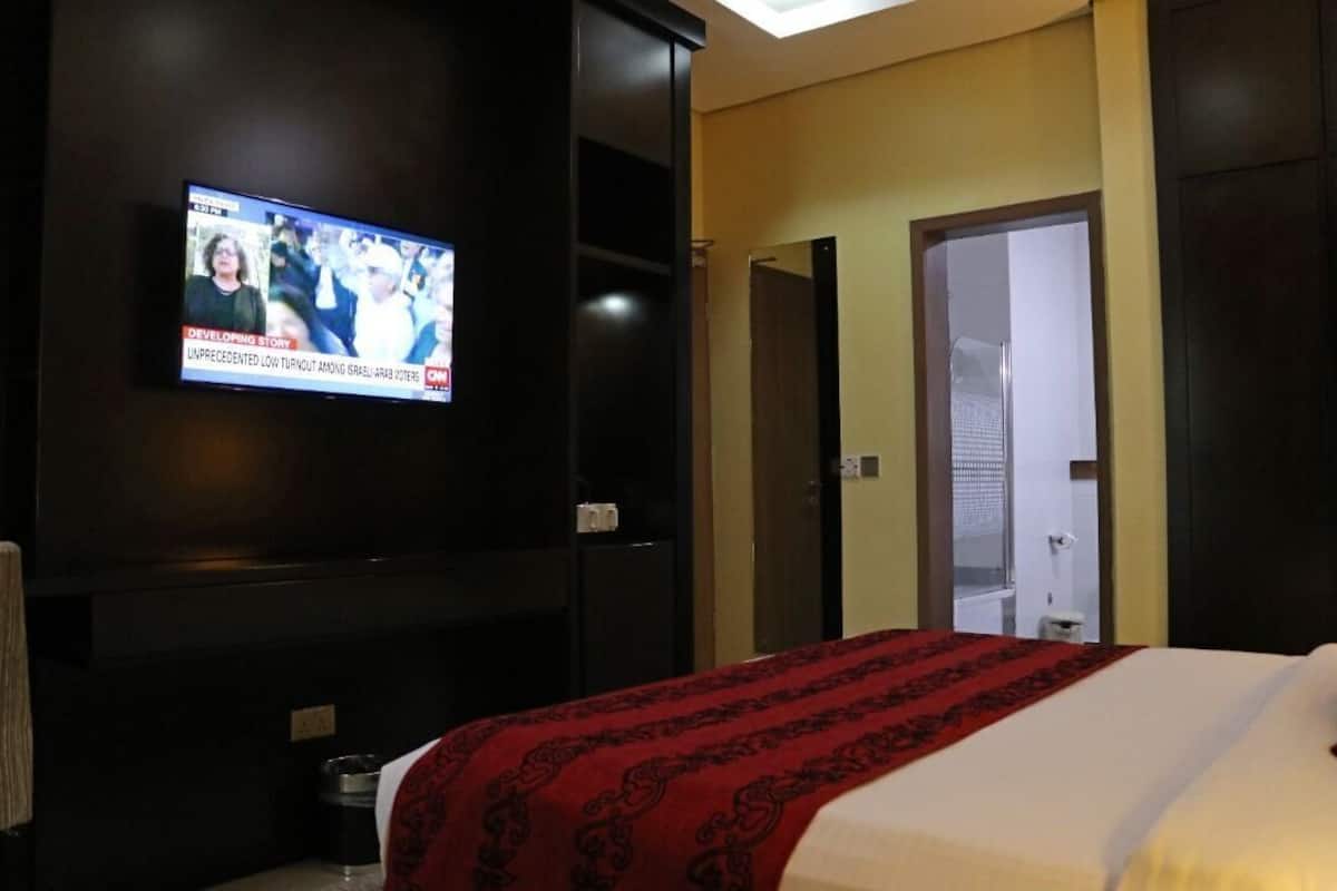 A hotel room with a bed, a TV mounted on the wall, and a door leading to a bathroom.