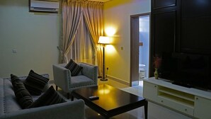 A living room with a sofa, armchair, coffee table, lamp, TV, and curtains. - Best Western Plus By Bayse-LTD (Ibadan)