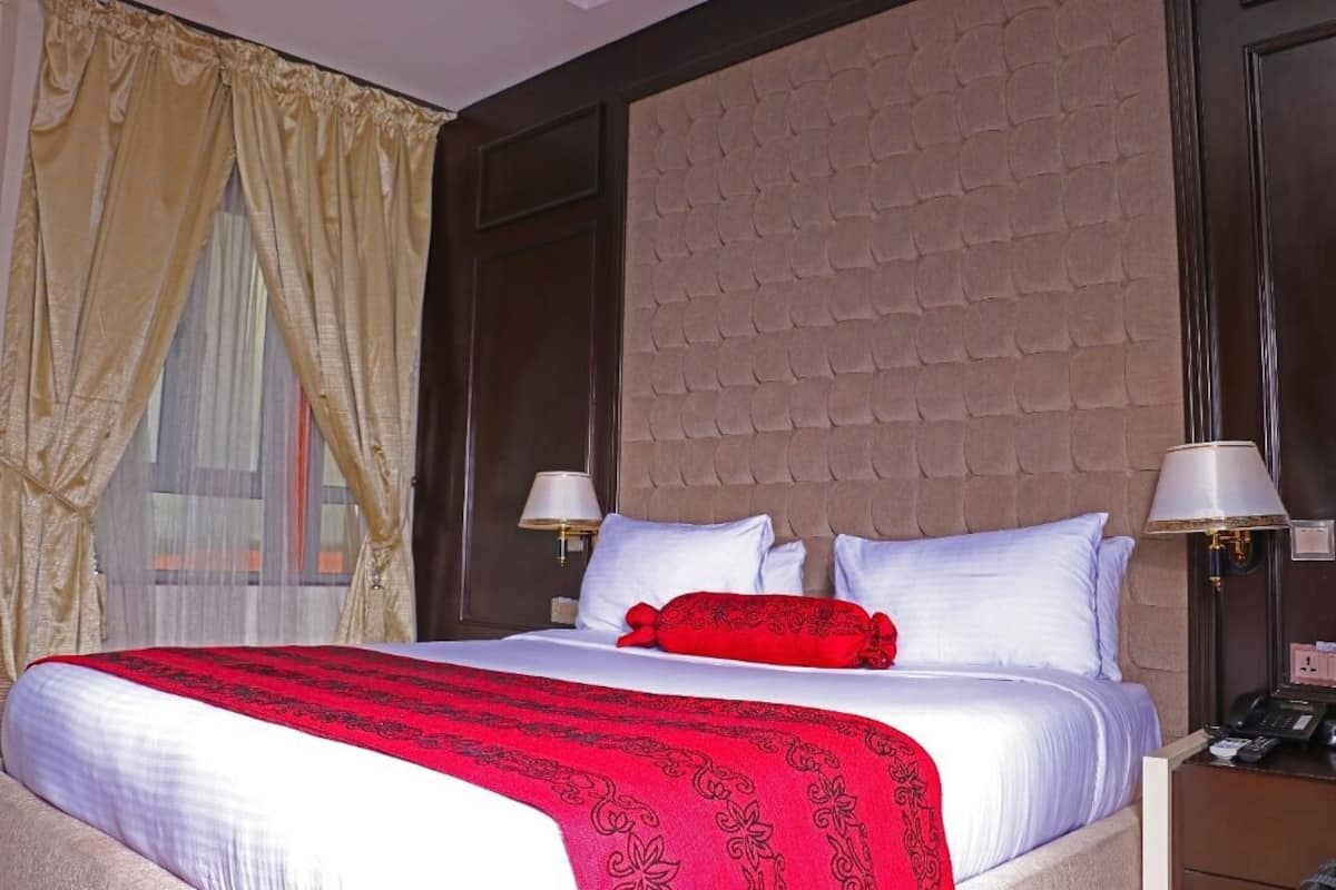 A hotel room with a large bed, two bedside lamps, a telephone, and a window with curtains.