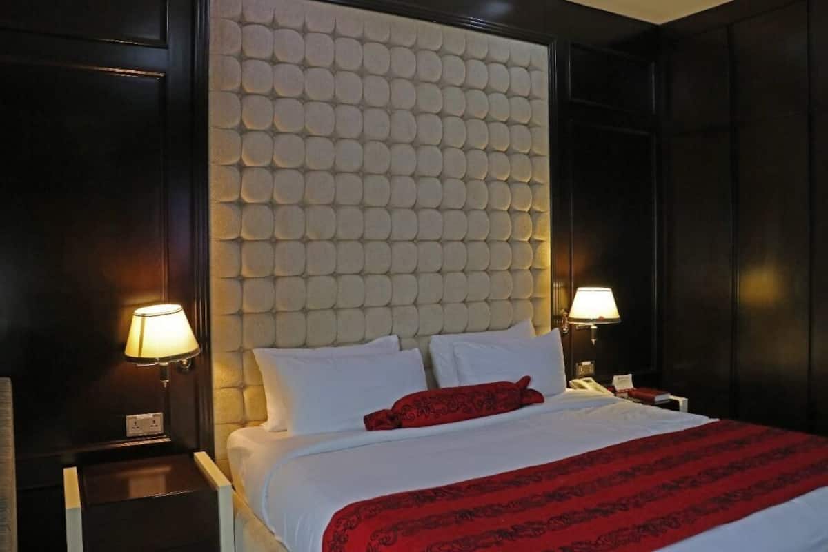 A hotel room with a tufted headboard, white bedding, a red throw pillow, bedside lamps, and a nightstand.