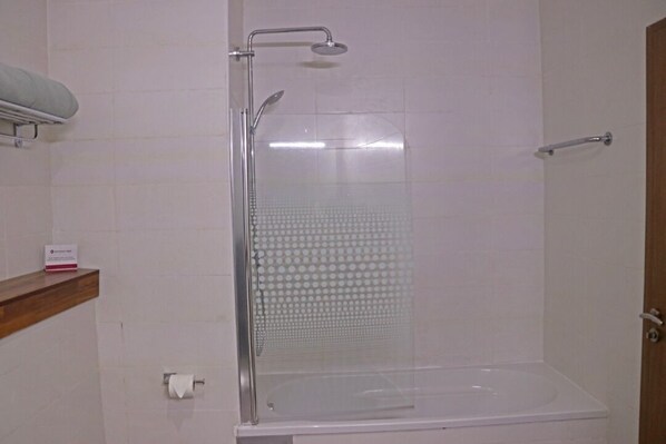 Cabina de ducha con puerta de vidrio, cabezal de ducha manual y toallero de pared.