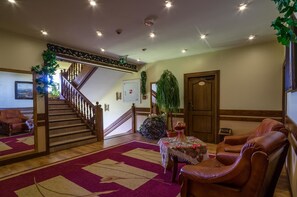 A spacious lobby with a wooden staircase, leather seating, a floral table, and a large plant. - Willa Roztoka (Bukowina Tatrzanska)