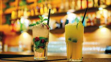 Two cocktails on a bar counter with a blurred background of bottles.