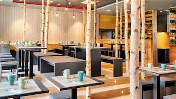 A modern restaurant with birch tree decor, wooden tables, and a TV screen.