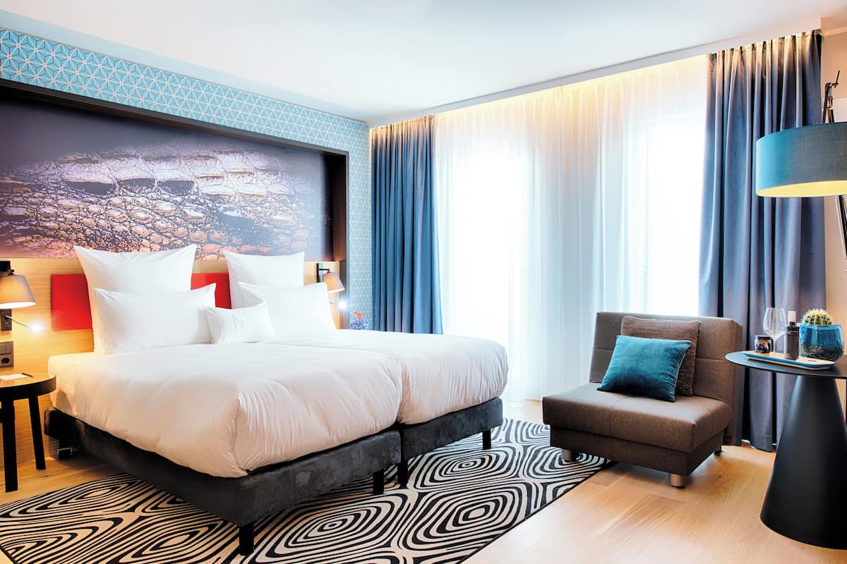 A modern hotel room with a large bed, a small sofa, a side table, and a lamp.