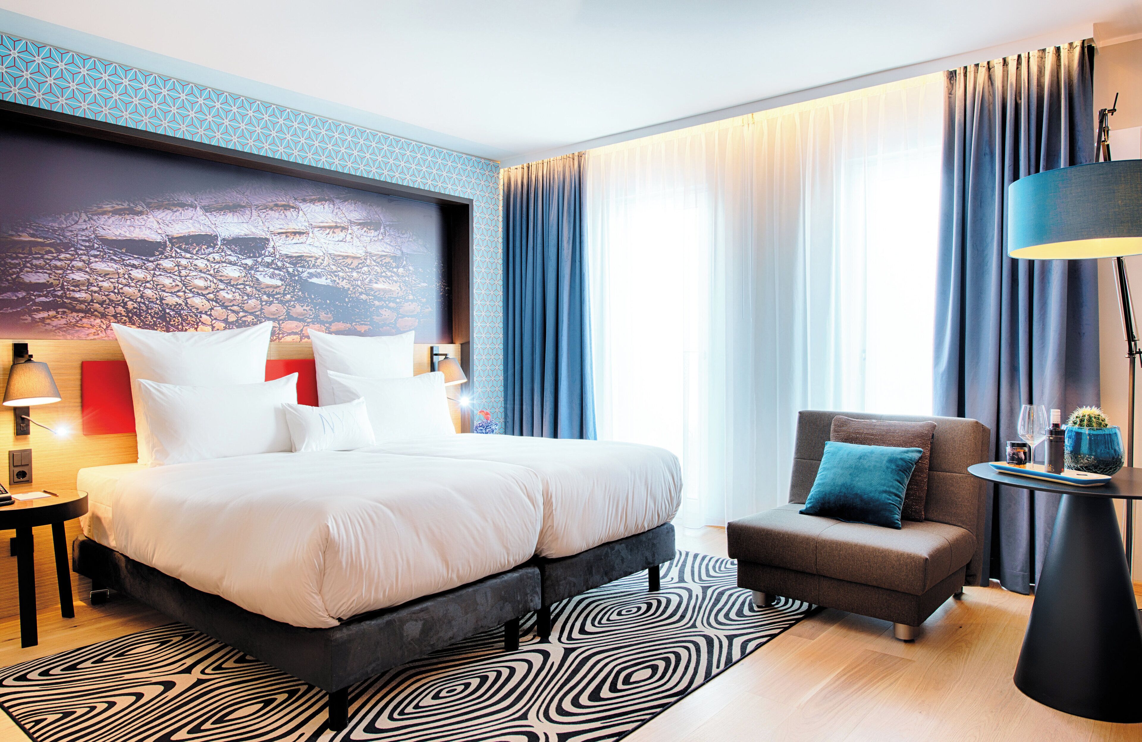 Ein modernes Hotelzimmer mit einem großen Bett, einer kleinen Couch, einem Beistelltisch und einer Lampe.