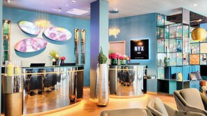 A modern hotel reception area with a blue wall, a reception desk, and seating area. - NYX Hotel Munich by Leonardo Hotels (Munich)