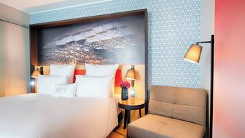 A hotel room with a large bed, a sofa, a nightstand with a lamp, and a wall with a geometric pattern.