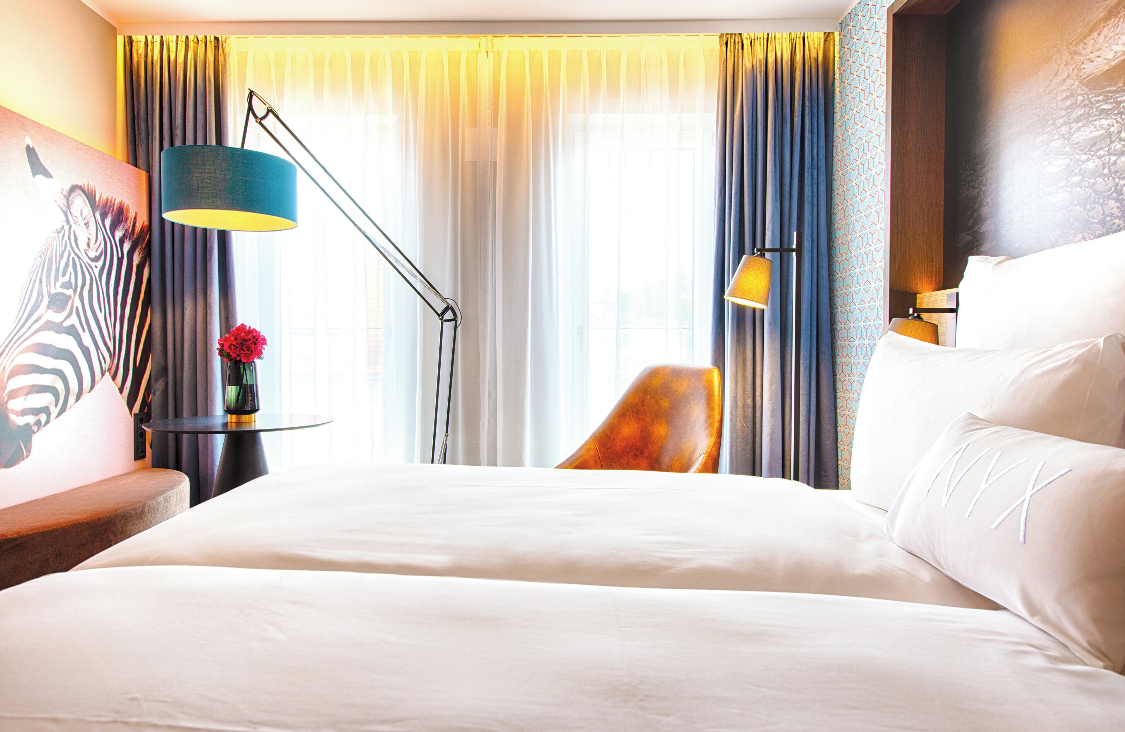 A hotel room with a large bed, a desk with a lamp, a chair, and a painting on the wall.