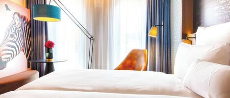 A hotel room with a large bed, a desk with a lamp, a chair, and a painting on the wall.