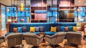 A modern living room with a blue sofa, multiple armchairs, and a large flat-screen TV. - NYX Hotel Munich by Leonardo Hotels (Munich)