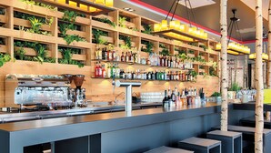 A bar area with shelves of bottles, a coffee machine, and seating. - NYX Hotel Munich by Leonardo Hotels (Munich)