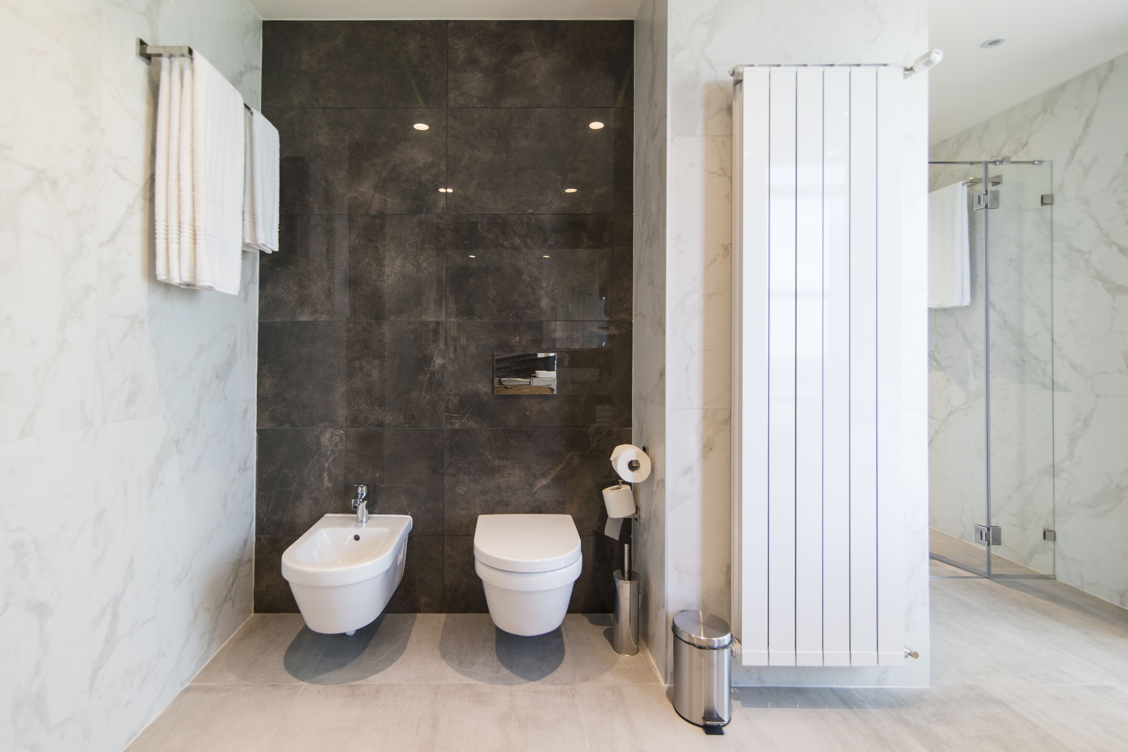 A modern bathroom with two bidets, a toilet, a trash can, and a shower area.