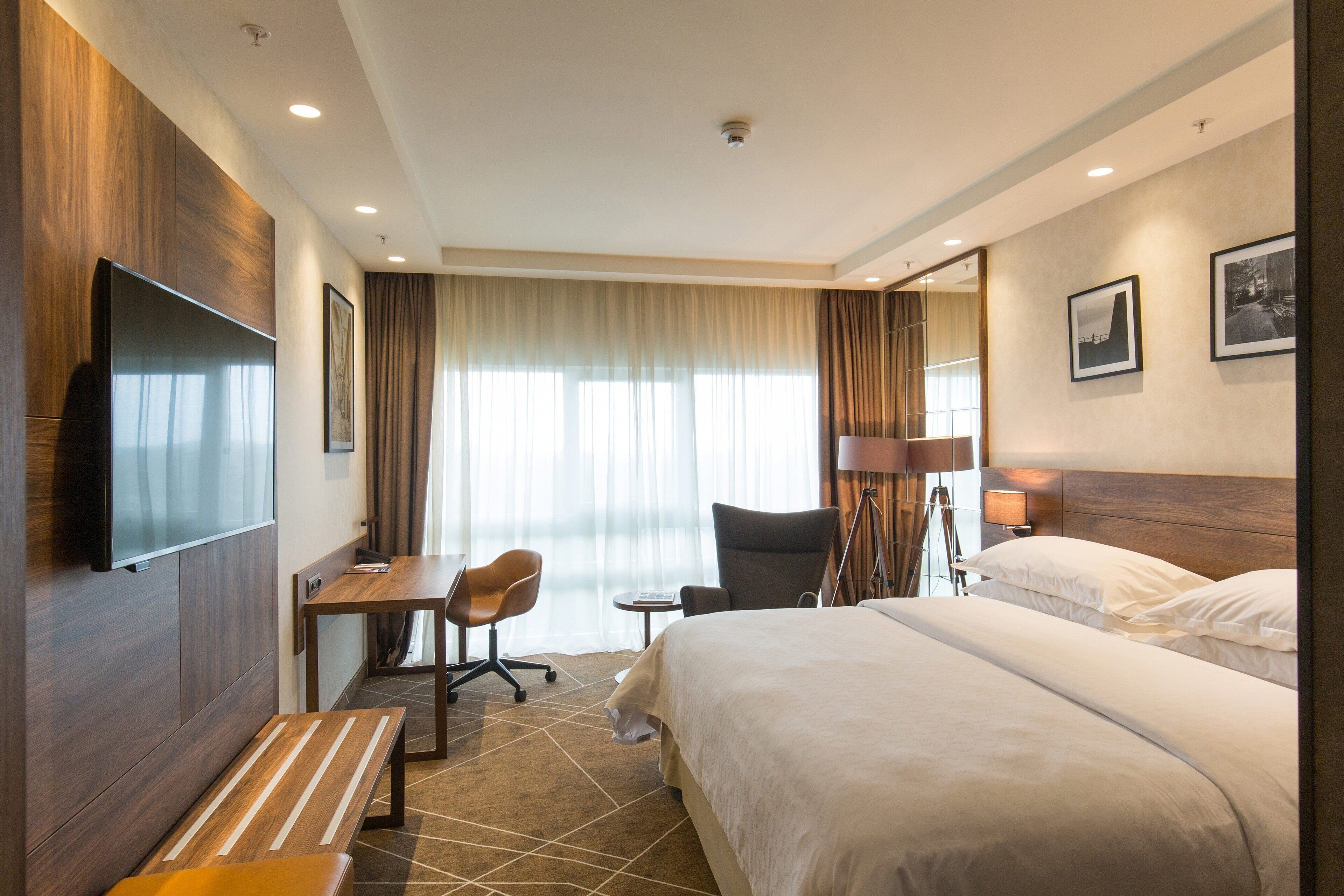 A hotel room with a large bed, a desk with a chair, a television, and a lamp.