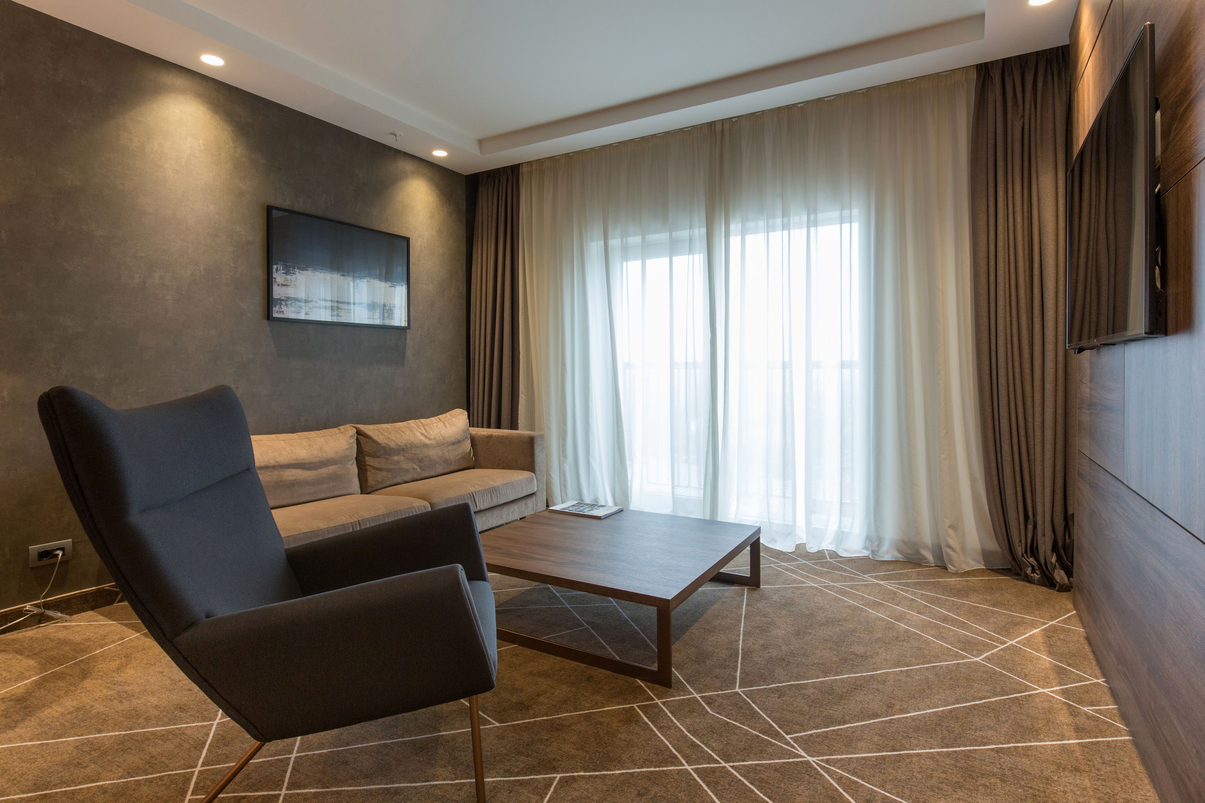 A modern living room with a sofa, a chair, a coffee table, and a large window with curtains.