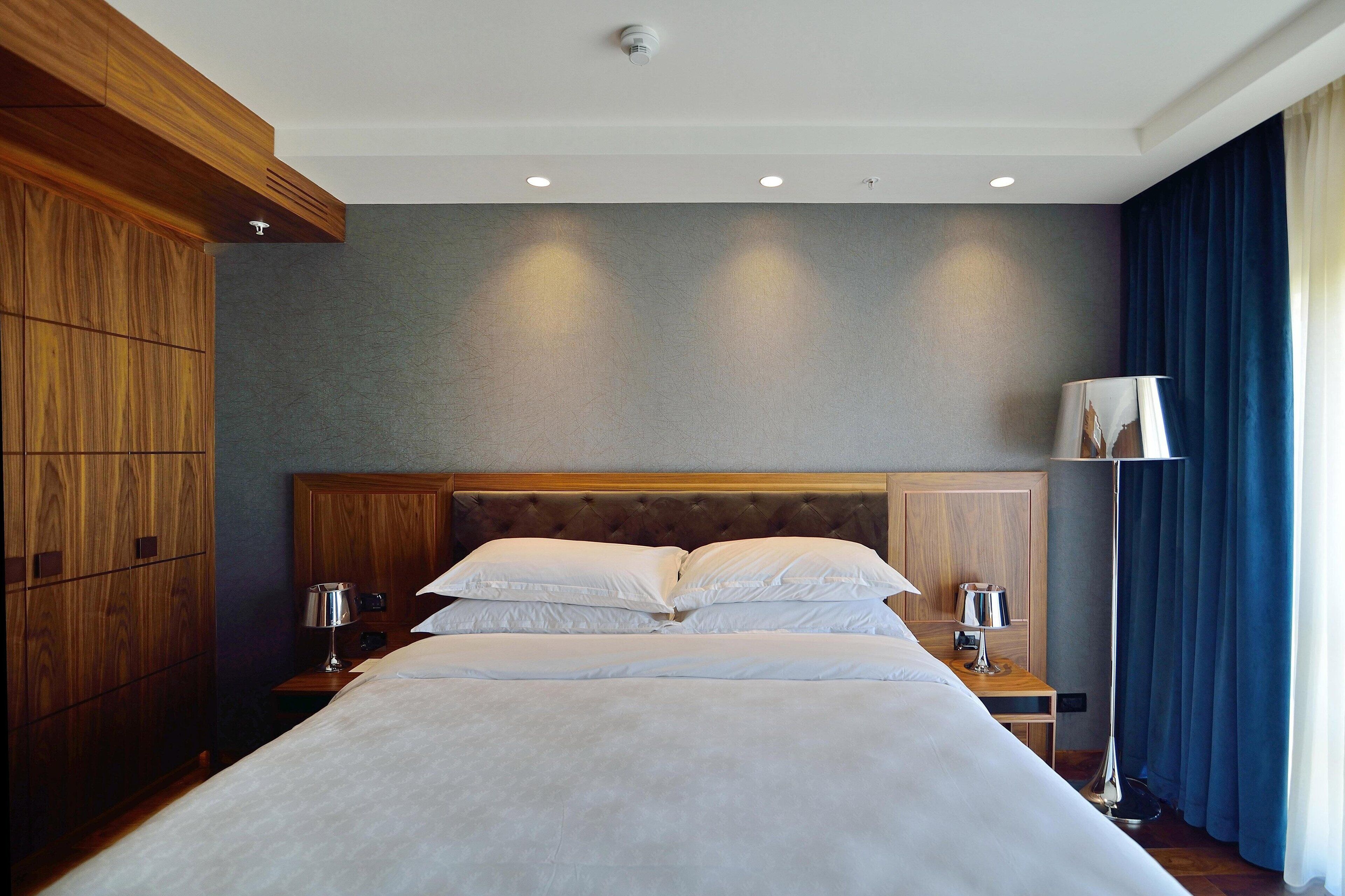 A hotel room with a large bed, wooden headboard, two bedside tables with lamps, and a floor lamp.