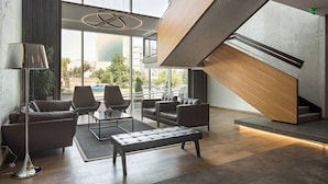 A modern lobby with leather sofas, a glass coffee table, and a staircase with a wooden finish. - Sheraton Novi Sad (Novi Sad)